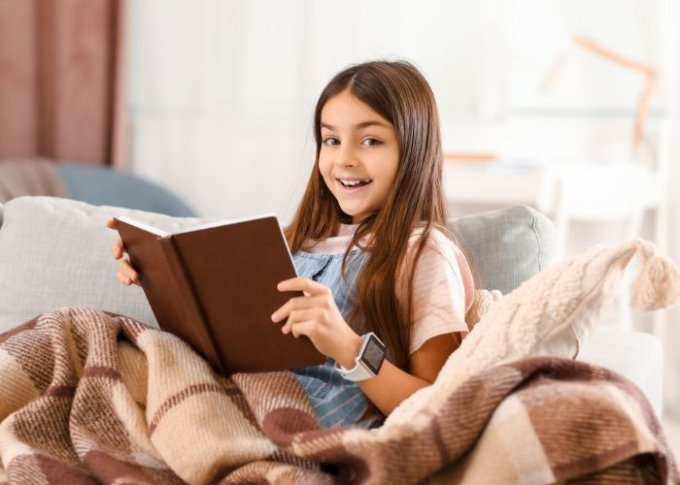 11 letnia dziewczynka czyta książkę ze smartwatchem na ręce